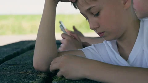 Young Boy Sitting Outdoors and Scrolling on Smartphone Stock Footage 339031741