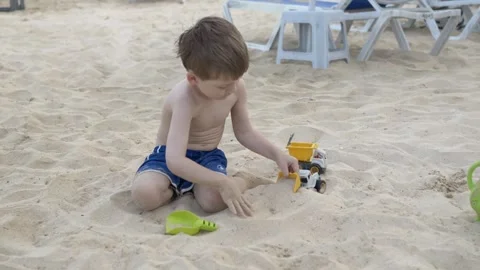 Young boy sitting on sand and playing with toy truck. Summer leisure and Video stock 317324005