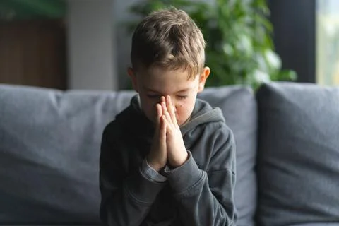 Young Boy Sitting on a Sofa With Hands Clasped in a Moment of praying Stock Photos