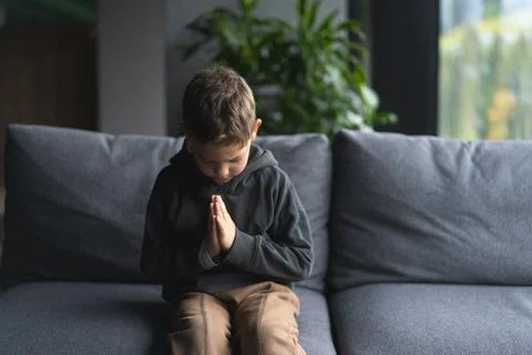 Young Boy Sitting on a Sofa With Hands Clasped in a Moment of praying Foto stock
