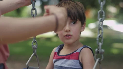 Young boy sitting on a swing with his mom getting him ready to swing Video stock 143619145