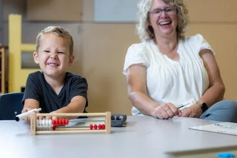 A young boy is sitting at a table with an abacus and smiling with his teacher Stock Photos