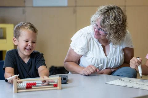 A young boy is sitting at a table with an abacus and smiling with his teacher Stock Photos