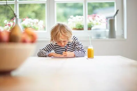 Young boy sitting at table drawing on paper Stock Photos
