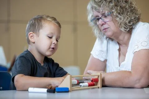 A young boy is sitting at a table with his teacher teaching him math Stock Photos