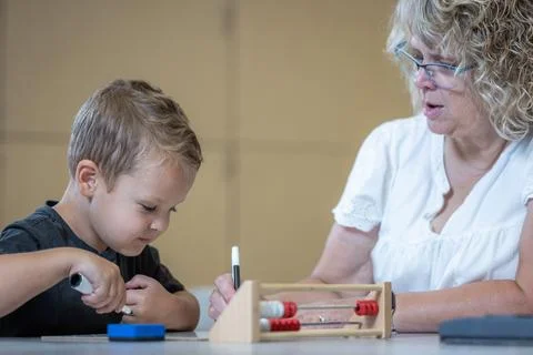 A young boy is sitting at a table with his teacher teaching him math 写真素材