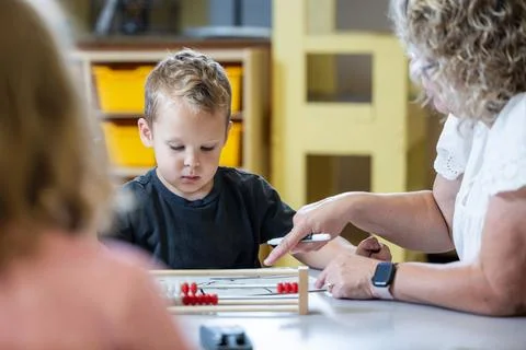 A young boy is sitting at a table with his teacher teaching him math Stock Photos