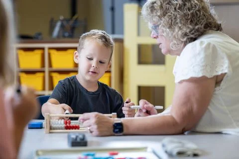 A young boy is sitting at a table with his teacher teaching him math Stock Photos