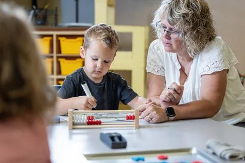 A young boy is sitting at a table with his teacher teaching him math Stock Photos