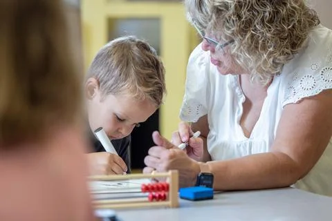 A young boy is sitting at a table with his teacher teaching him math Stock Photos