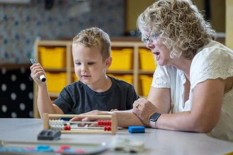 A young boy is sitting at a table with his teacher teaching him math 写真素材