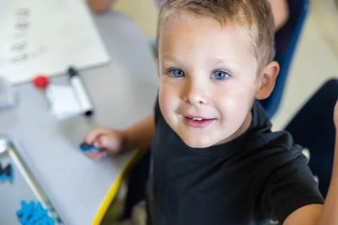 A young boy is sitting at a table with a white board behind him Foto stock
