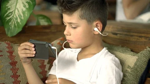 Young boy sitting in tropical cafe and watching cartoon on smartphone, steadycam 動画素材 81090622
