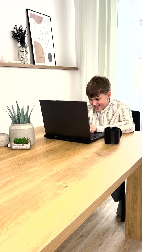 A young boy is sitting, working at his laptop and looking at the laptop screen Stock Footage 272751401