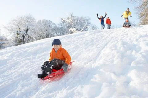 Young boy sledging down hill with family watching Stock Photos