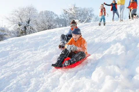 Young boy sledging down hill with family watching Stock Photos