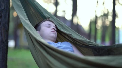 A young boy sleeps peacefully in a green hammock among forest trees.  Stock Footage 338415819