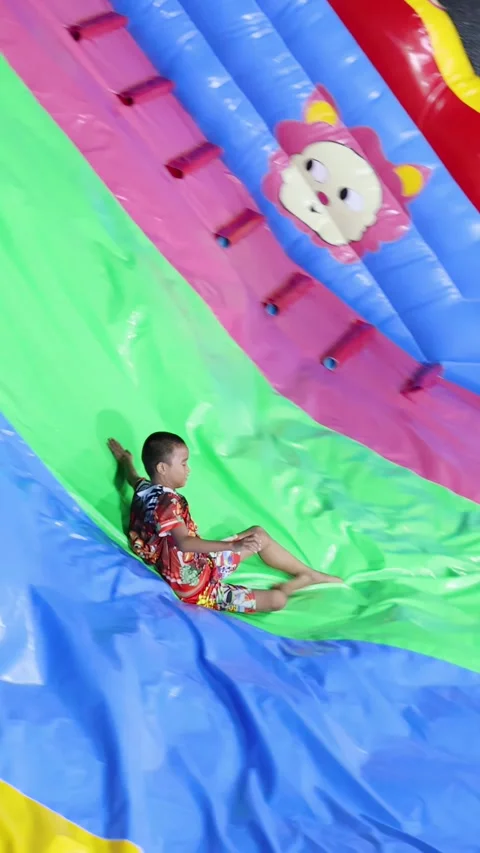 Young Boy Sliding Down Colorful Inflatable Slide at Amusement Park Stock Footage 328147681