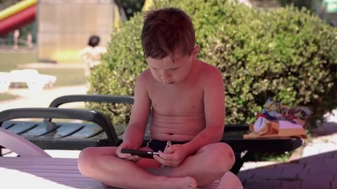Young Boy With Smartphone or Tablet Sitting in neatr the Pool on a chair. Play Stock Footage 80687129