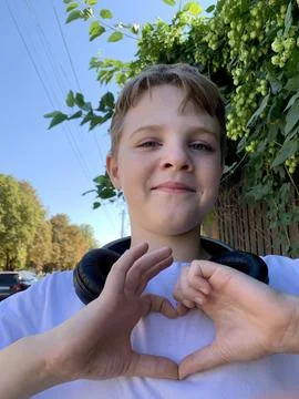 A young boy smiles brightly while forming a heart shape with his hands. He wears Stock Photos