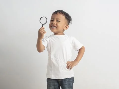 Young boy smiles joyfully while holding a magnifying glass high. White tshi.. Photos