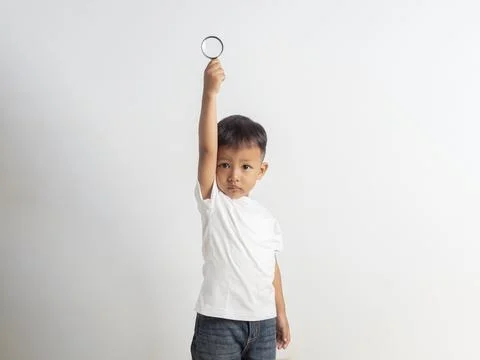 Young boy smiles joyfully while holding a magnifying glass high. White tshi.. Stock Photos