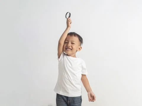 Young boy smiles joyfully while holding a magnifying glass high. White tshi.. 스톡 사진