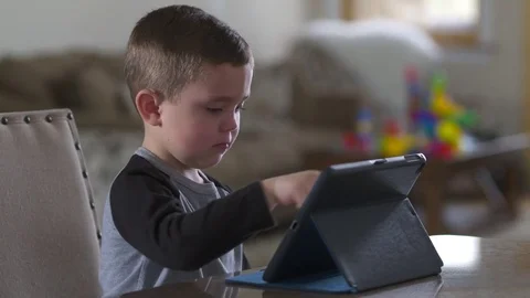 Young boy smiles while looking for videos on his tablet from kitchen counter Stock Footage 85366192