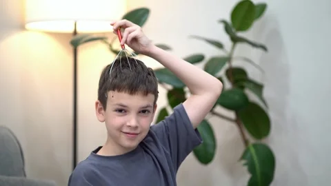 Young boy smiles while using a head massager on his scalp at home. Stock Footage 340174947
