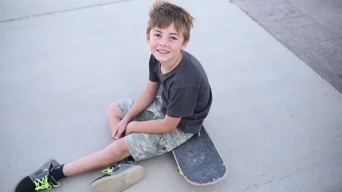 Young boy smiling at camera while sitting on a skateboard Stock Footage 94930316