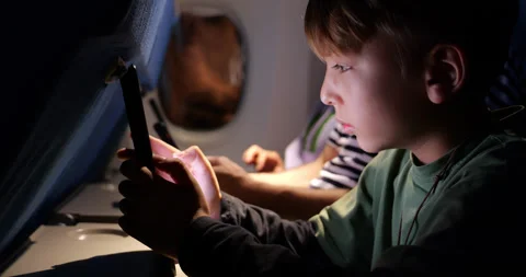 Young boy solving puzzle at tablet during night flight, close side view Stock Footage 303992504
