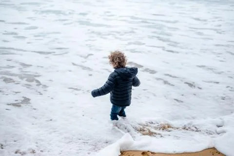 Young boy splashes in the surf fully clothed in winter Foto stock