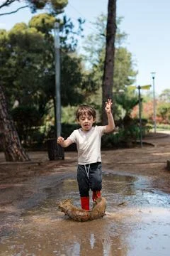 Young boy splashing in mud puddle wearing red boots Fotos de archivo