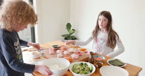 Young boy spoons rice from a serving bowl while a young girl uses chopsticks Stock-Footage 115545505