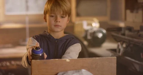 Young boy is spraying blue paint on wood Stock Footage 85892872