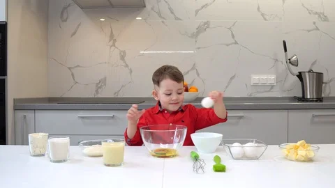 Young boy standing breaking fresh eggs into a bowl as he prepares to make batter Video stock 128833425
