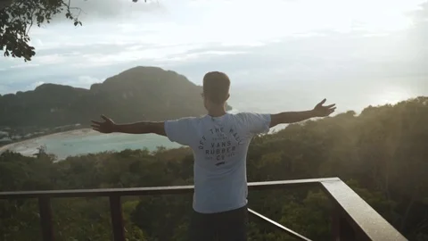 Young boy standing on the edge of a view point looking at tropical island's suns Stock Footage 125390157