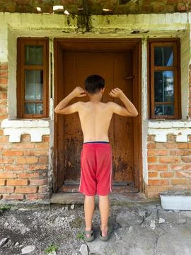 A young boy standing in front of a brick building with his back to the camera Stock Photos
