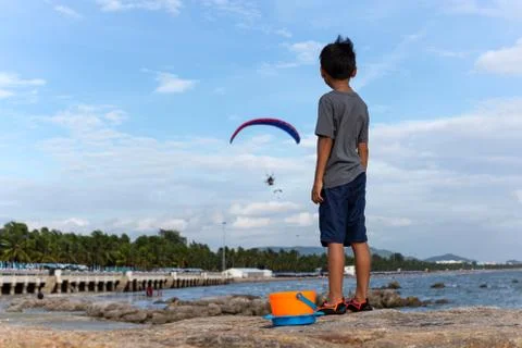 Young boy standing on the rock looking at motor paraglider flying on the beac Foto stock