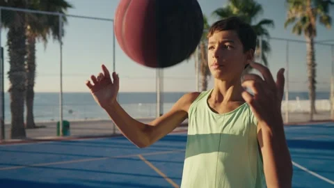 Young boy stands and juggles ball on finger on basketball court against blue sky Stockbeeldmateriaal 209519378