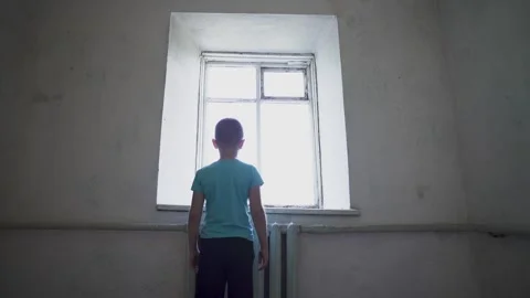 A young boy stands in the corner of an empty, old room. Alone kid. Stock Footage 314135144