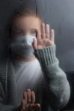 A young boy stands at the window with a raindrop on the glass after the rain. Stock Photos