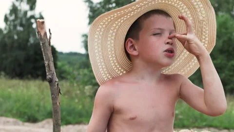 Young boy in straw hat playing with stick in lush green countryside. Stock Footage 287524944