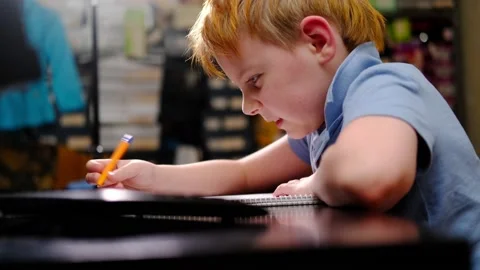 A young boy is studying hard at the table at home. He writes with a pen in a  Vidéo 171629108