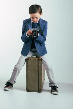 Young boy in suit with camera sitting on suitcase Stock Photos