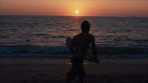 Young boy surfs the waves of tropical sandy beach while the Sun sets behind Stock Footage 119116147