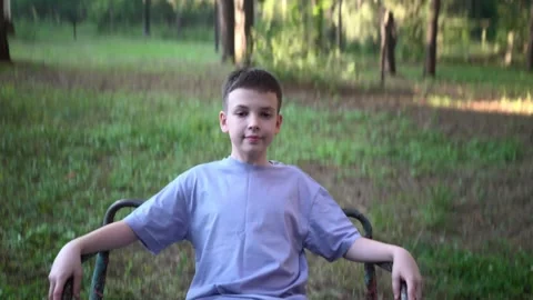 Young boy swinging gently on a swing in a serene forest.  Video stock 342179328