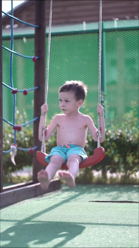 Young boy swinging joyfully on a red swing at sunny outdoor playground. Vídeo Stock 342193034