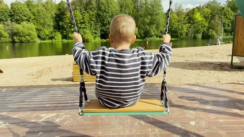 A young boy swings peacefully while admiring the lake view. Video stock 344985753
