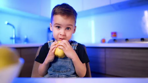 Young boy taking a bite of yellow apple. A child holds fresh fruit with both Stock Footage 342573928